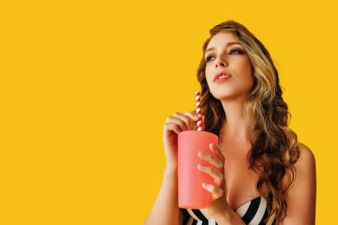 Sarı arka planda bir fincan kahvesi olan güzel genç bir kadın.