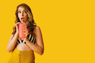 Genç ve güzel bir kadın bir fincan kahve tutuyor ve sarı arka planda dururken şaşırmış görünüyor.