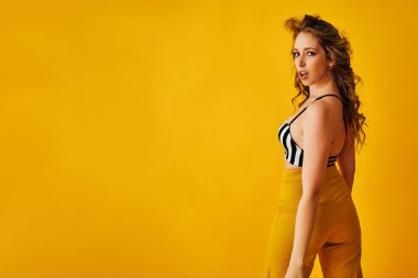 Siyah mayo giymiş, kolları sarı arka planda çapraz duran güzel bir genç kız.