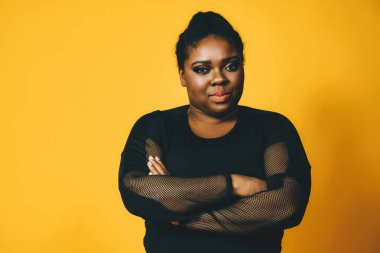 Sarı arka planda çapraz kollu güzel bir Afrikalı Amerikalı kadının portresi.