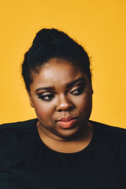 Afro saçlı güzel bir Amerikalı kadının portresi, sarı bir arka planda izole edilmiş.