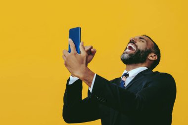 Sarı arka planda akıllı telefonu ve cep telefonu olan takım elbiseli yakışıklı sakallı bir adamın portresi.