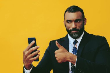 Sarı arka planda telefonu olan takım elbiseli yakışıklı sakallı bir adamın portresi.