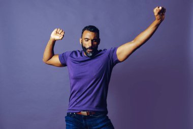 Mor arka planda mavi tişörtlü, sakallı bir gencin portresi.