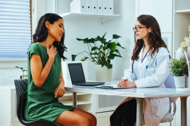 sick female patient explaining illness to woman doctor at consultation clinic during healthcare checkup