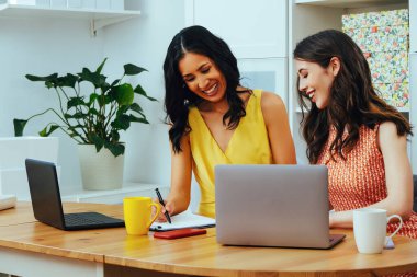 Businesswoman looking at note pad and smiling while sitting at modern office with laptop business