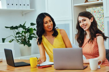 Businesswoman looking at camera and smiling while sitting at modern office with laptop