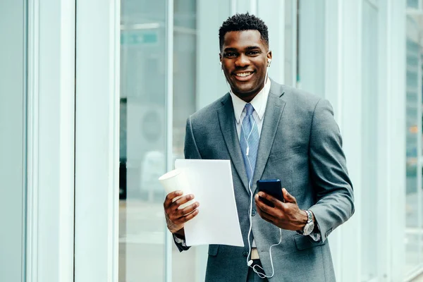 Positive young entrepreneur using smartphone outside wearing suit and tie