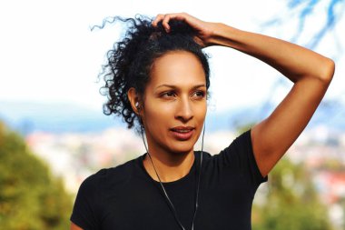 Kulaklıklı, kıvırcık saçlı spor kıyafetli bir kadın.