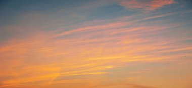 Bulutlu, güneşli, gün batımlı, batan güneşin turuncu-sarı tonlarıyla gökyüzünün fotoğrafı.