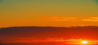 Bulutlu, güneşli, gün batımlı, batan güneşin turuncu-sarı tonlarıyla gökyüzünün fotoğrafı.