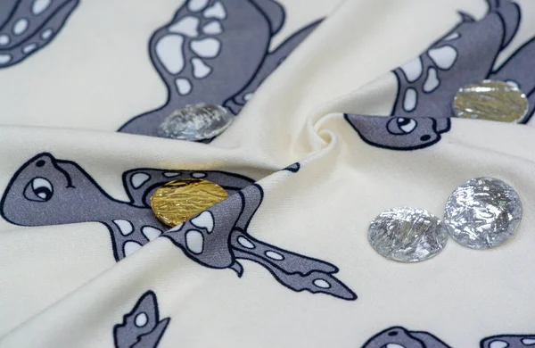 Cotton, Jersey. White background with a print of gray turtles. Sew-on rhinestones. Jersey is a plain knit cotton fabric known for its elasticity and softness.