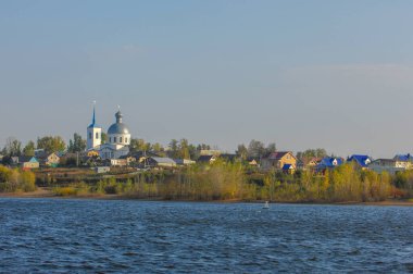 Sonbahar manzarasının fotoğrafı, nehir kıyısındaki sarı ağaç yaprakları, güneşli bir günde mavi gökyüzü ve beyaz bulutların arka planına karşı, suya yansıyor.