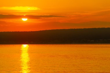 Yazın nehrin üzerinde gün batımı. Muhteşem sıcak hava çarpıcı günbatımına katkıda bulundu. Nehirdeki su tamamen hareketsiz. Kızıl gökyüzü. İnanılmaz renklerde bir suya yansıyor..