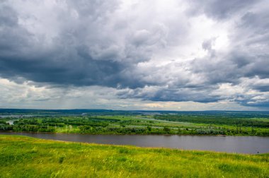 Yaz manzarası, büyük bir nehir, nehrin kıyısında çayır çiçekleri, gökyüzünde güçlü bulutlar, Kama Nehri boyunca bir turist yürüyüşü.