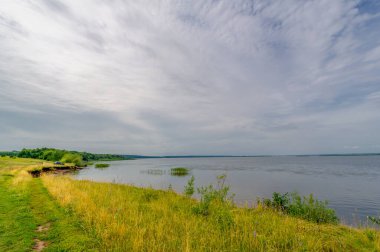 The floodplain of a large river is covered with green vegetation. Dirt road of local importance. Beautiful blue sky. Summer landscape photography. European part of the land. fields, meadows, ravines.