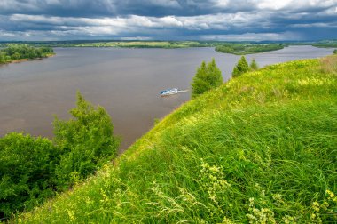 Yaz manzarası, büyük bir nehir, nehrin kıyısında çayır çiçekleri, gökyüzünde güçlü bulutlar, Kama Nehri boyunca bir turist yürüyüşü.