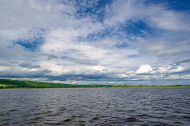 summer photo on a large deep river, powerful storm clouds, blue sky, dark harsh water, tourist walk along the Kama river