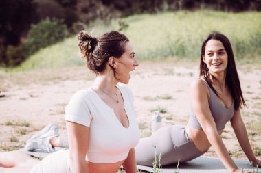 Twp women in workout clothes laughing while practicing Pilates or yoga outdoors