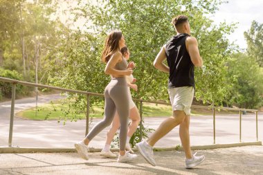 Three millennial friends jogging in a park with warm sunlight in the background