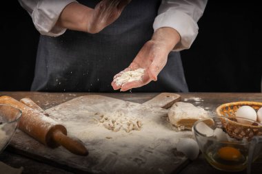 Kadın eli, un ve hamur. Ev yapımı pişirme hamuru pişiren önlüklü bir kadın. Ev yapımı, sade bir atmosfer. Sıradışı ışıklandırması olan karanlık bir arka plan..