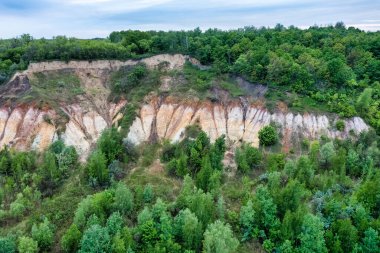 Colorful clay hills overgrown with green trees. Natural abstract landscape, aerial view, from drone
