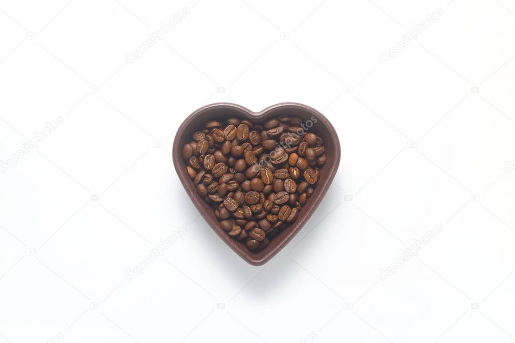 Roasted coffee beans in heart shaped bowl on white background. Love coffee concept. Top view flat lay with copy space