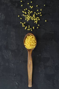 Siyah arka planda tahta kaşıkta çiğ makarna farfalle. İtalyan mutfak malzemelerinin üst görünümü.