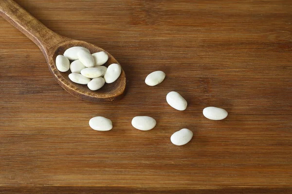木製のスプーンで白い豆は 木製の背景にクローズアップ ベジタリアンフード — ストック写真