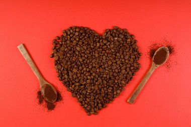 Kalp kahvesi. Parlak kırmızı arka planda kalp şeklinde kavrulmuş kahve çekirdekleri. Kahve aşkı kavramı, Sevgililer Günü, iyi ruh hali, hediye. Tahta kaşıkla.