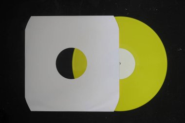 Beyaz kağıt kapağı ve sarı plak plağı siyah arkaplanda izole edilmiş.