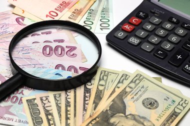 Banknotlar bir hesap makinesi ve büyüteç ile bir masaya yayılmış.