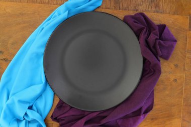 Empty black slate plate on wooden table. Food background for menu, recipe. Table setting. Flatlay, top view. Mockup for restaurant dish