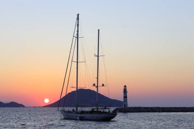 Bodrum, Hindi. 14 Ağustos 2022: Gün ışığında deniz manzarası. Deniz feneri ve sahilde yelkenliler. Deniz kenti Turgutreis ve muhteşem güneş ışığı