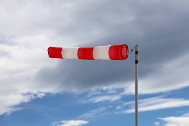 Bulutlu gökyüzünde kırmızı ve beyaz rüzgarlık göstergesini kapat