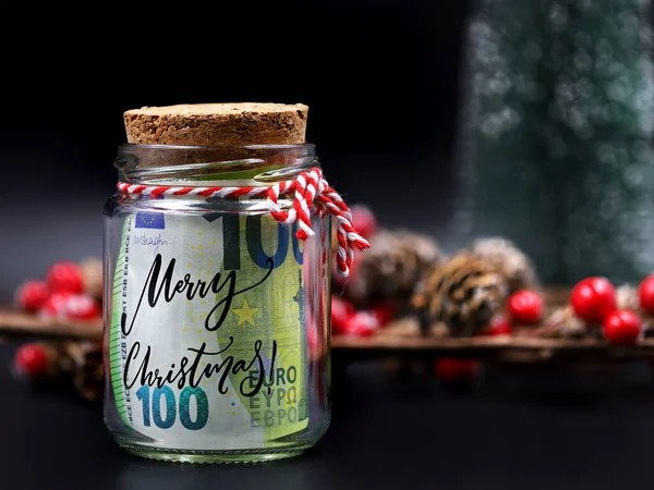 Yılbaşı kavanozunda Avro para banknotu. Siyah arka planda mutlu noeller ve noel süslemeleri.