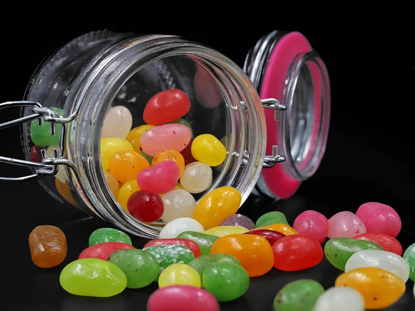 Скляна банка барвистих желевих бобів, розлитих на чорному фоні — стокове фото