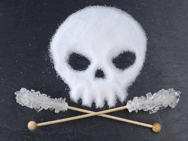 Czaszka w kształcie z rafinowanego cukru białego i skrzyżowanego cukru cukierkowego na drewnianych patykach na czarnym tle łupkowym, śmiertelne ryzyko nadmiernego spożycia cukru — Zdjęcie stockowe