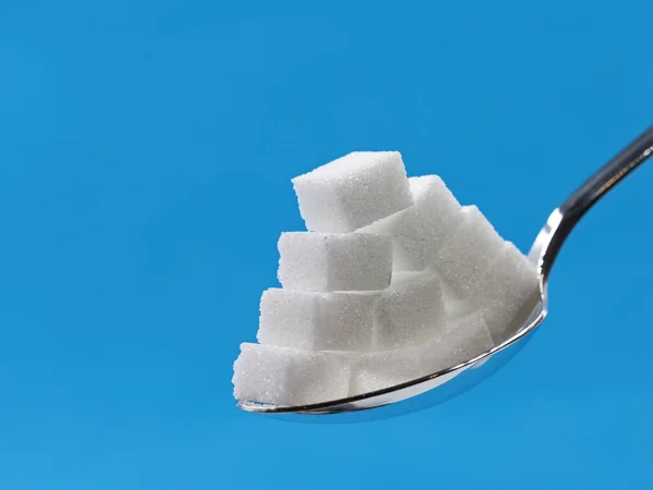 Piramida kostek cukru na srebrnej łyżeczce wyizolowana na niebieskim tle z przestrzenią do kopiowania — Zdjęcie stockowe