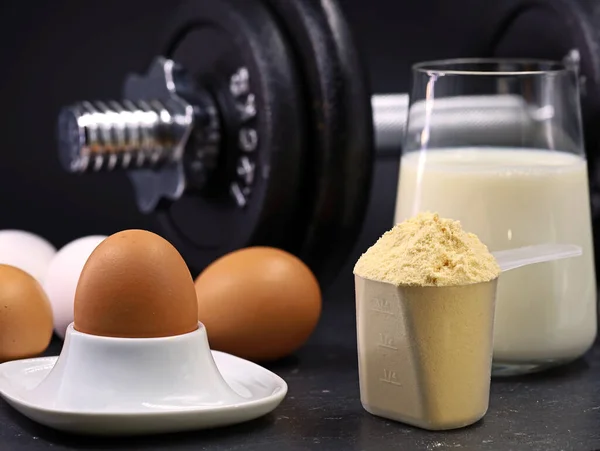 Yumurtalar, bir kepçe süt tozu, bir bardak süt ve siyah zemin üzerinde dambıl, yüksek protein içerikli spor beslenme konsepti