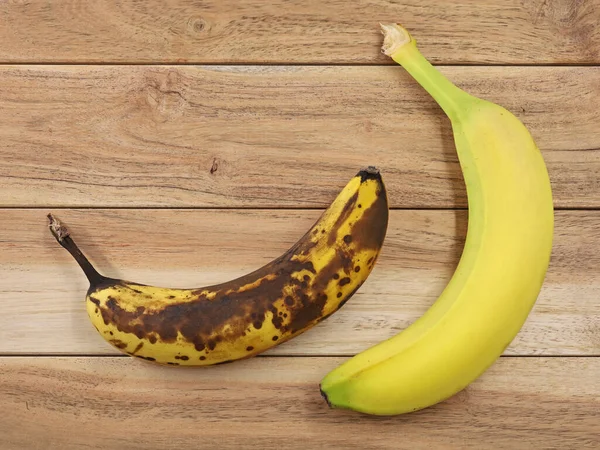 Верхний вид коричневого перезрелого и желтого спелых бананов на деревянном фоне, сравнение бананов — стоковое фото