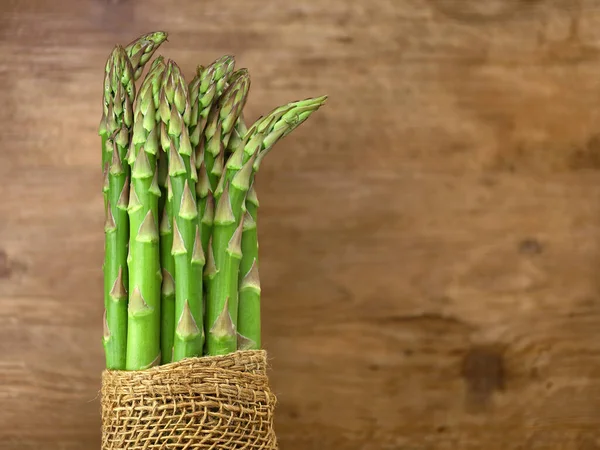 Bund frischer grüner Spargel auf braunem rustikalem Holzgrund mit Kopierraum — Stockfoto