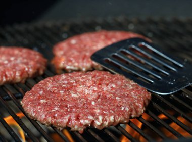 Izgarada taze çiğ biftek ızgarası ve arka planda paslanmaz çelik spatula.