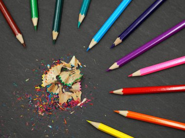 sharpened colored pencils with colorful shavings on black slate background, top view