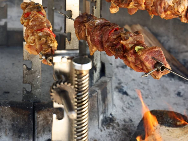 close up of seasoned cuts of meat on a rotisserie rolling over a wooden fire.