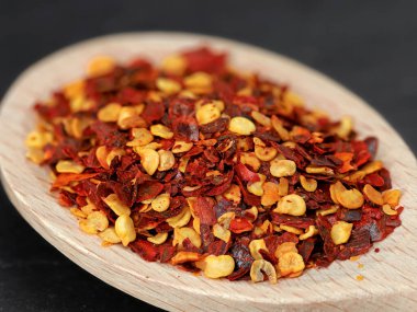 close up of red pepper flakes in wooden cooking spoon, hot ingredient for spicy foods.