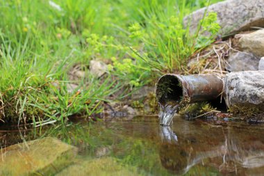 crystal clear water pouring from a metal pipe in the mountains.