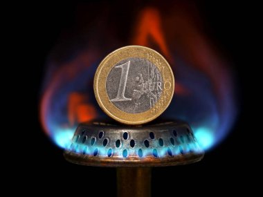 Close up of a one euro coin on top of a blue flame gas burner, concept imgage showing rising gas prices and energy costs in the European Union.