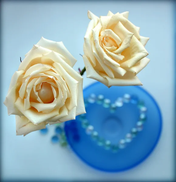 Dos rosas blancas con un corazón de cuentas de vidrio en la placa de vidrio azul —  Fotos de Stock