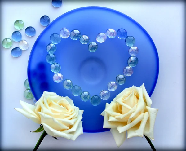 Dos rosas blancas con un corazón de cuentas de vidrio en la placa de vidrio azul — Foto de Stock